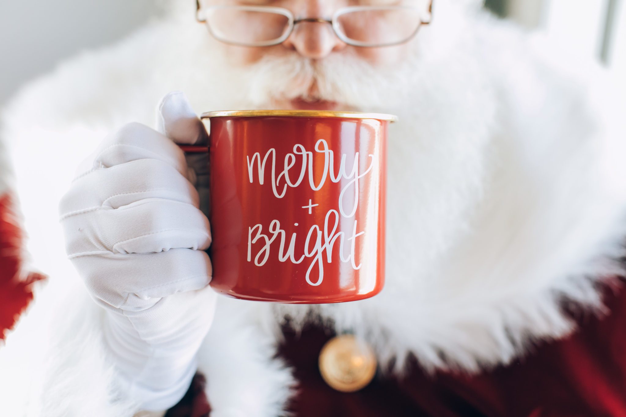 closeup of Santa Claus holding a red Merry + Bright Christmas mug
