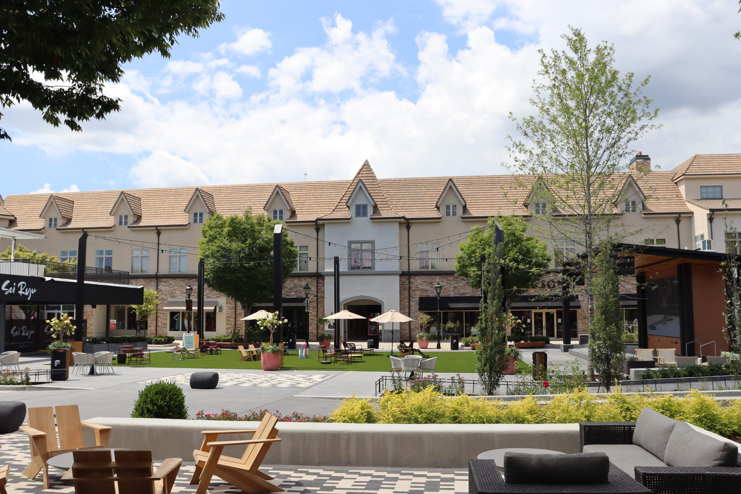 Outdoor green space with seating areas surrounded by trees and restaurants at The Forum.